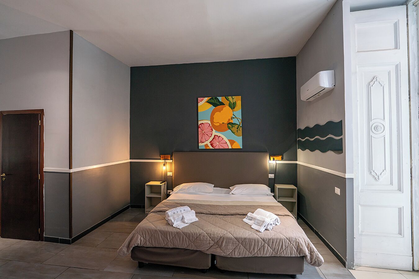 Ein Hotelzimmer mit einem Bett, Nachttischen, einem Gemälde und einer Klimaanlage.