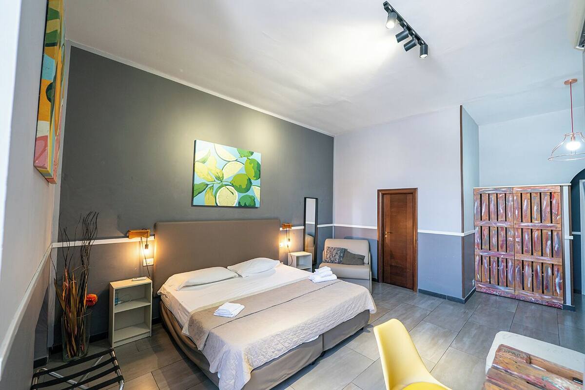A modern hotel room with a large bed, bedside tables, a mirror, a painting, and a wooden door.