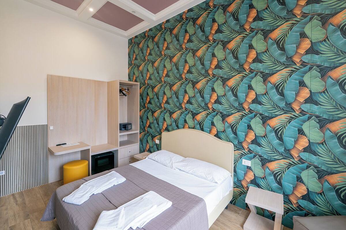 A modern hotel room with a bed, a desk, and a wardrobe.