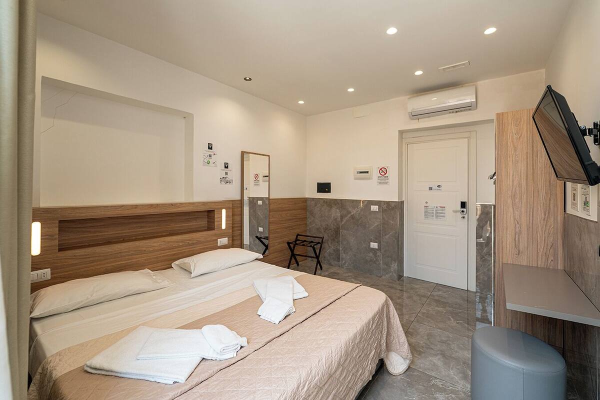 A hotel room with a bed, a chair, a TV, and a bathroom door.