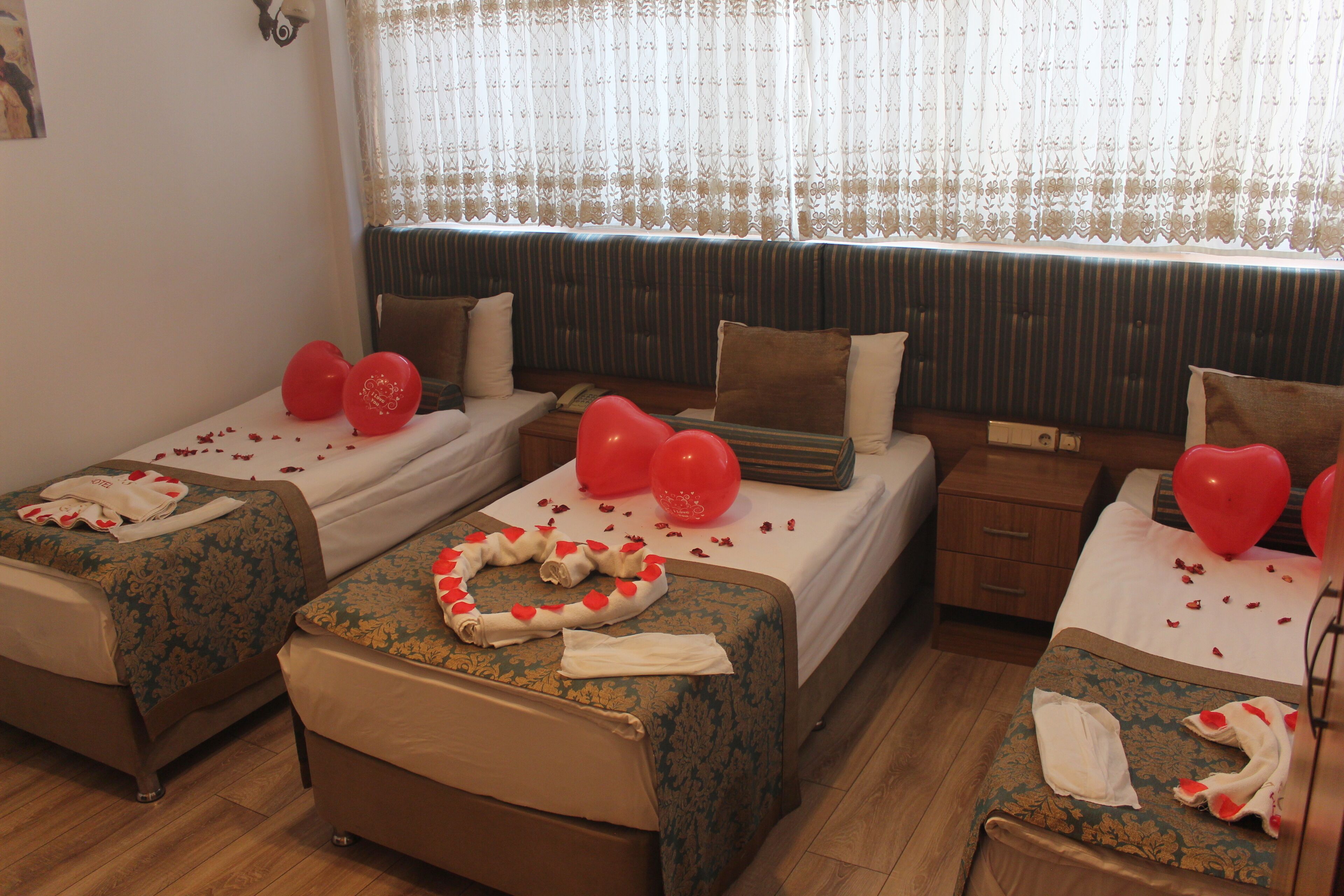 Quarto de hotel com duas camas de solteiro, cada uma com colcha floral, travesseiros e balões em formato de coração vermelho.