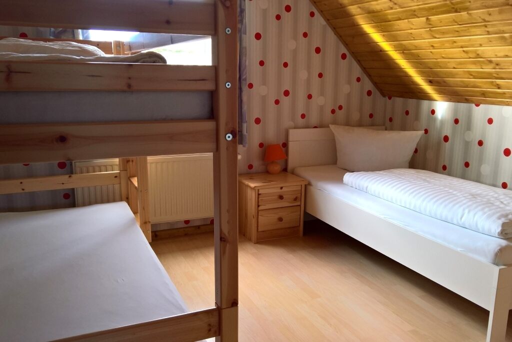 Une chambre de type dortoir, avec des lits superposés, un lit simple, une table de chevet et une lampe.