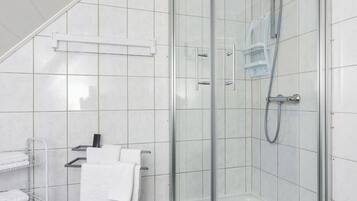Moderni kylpyhuone, jossa on lasiseinällä varustettu suihku, valkoisilla laatoilla päällystetyt seinät ja metallinen pyyhekoukku.