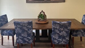 Een eethoek met een houten tafel en stoelen, een plafondventilator en een lijst met een schilderij aan de muur.