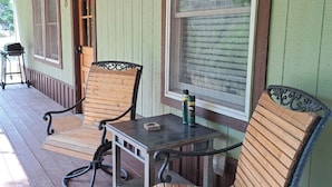 A covered porch with wooden chairs and a table, a grill, and a door with a window.