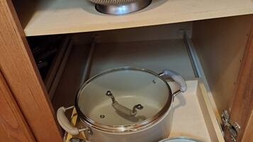 Un armario de cocina con un colador de metal, una olla de acero inoxidable con tapa y una sartén con tapa.