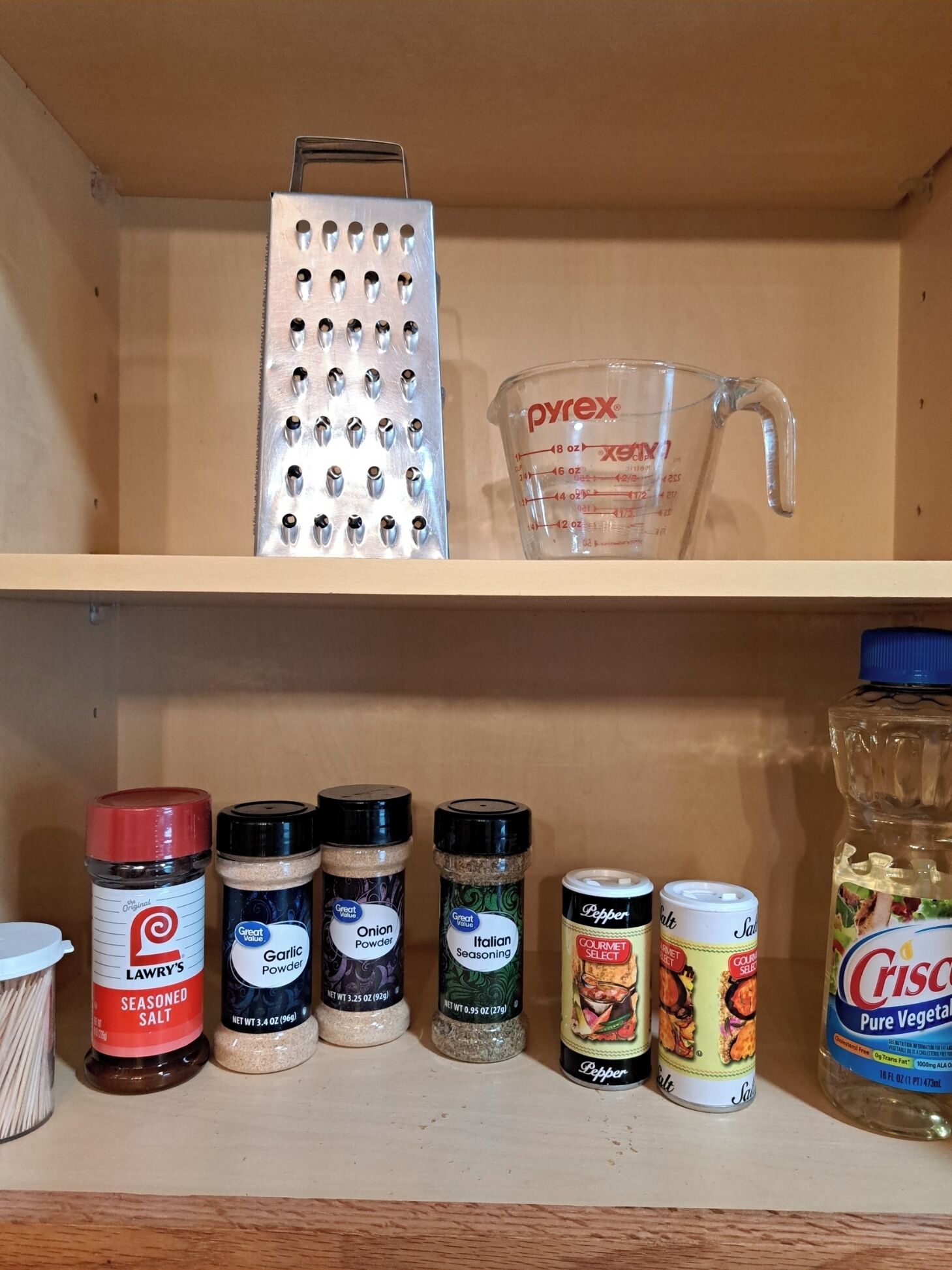 Uno scaffale in cucina con una grattugia, un misurino e diversi vasetti di spezie.