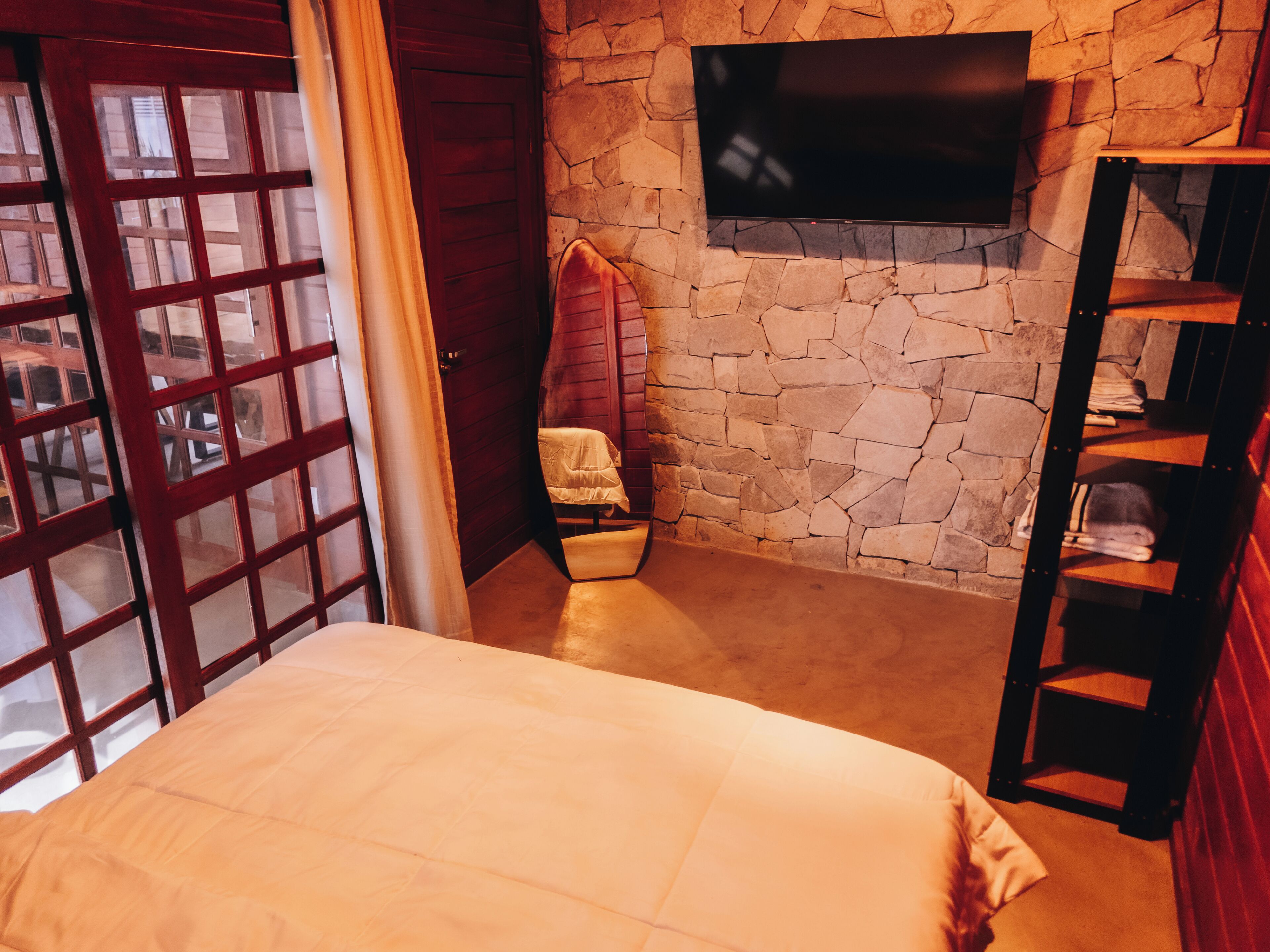A bedroom with a stone wall, a mounted TV, a wooden door, and a bed.
