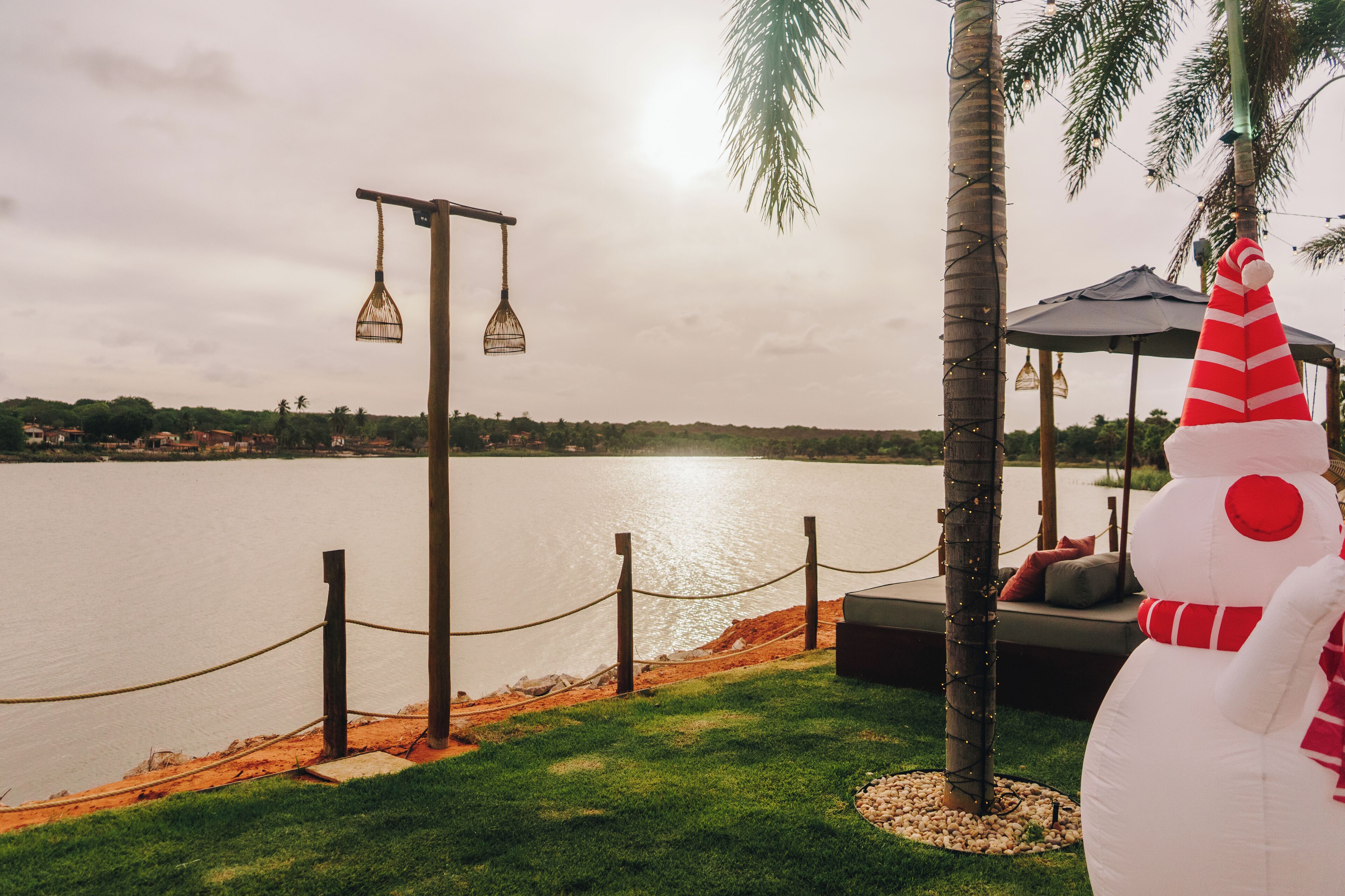 A view of a lake with a wooden fence and a gazebo with a snowman decoration.