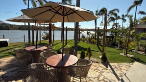 An outdoor seating area with wicker chairs and tables, surrounded by palm trees and a view of the lake. - Lagoon Paradise (Fortim)