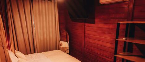 Una habitación con cama, repisas con toallas dobladas, aire acondicionado de pared y cortina.