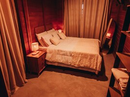 Un dormitorio acogedor con cabecera de madera, cama con ropa de cama blanca, mesita de noche con lámpara y banco de madera.