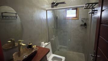 A bathroom with a glass-enclosed shower, a wooden vanity with a bowl sink, and a toilet.