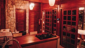 A kitchen with a stone wall, wooden cabinets, a stove, and a dining area with a table and chairs. - Lagoon Paradise (Fortim)