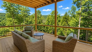 A covered deck with wicker furniture and a view of a forest.