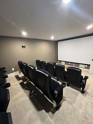Une salle de cinĂ©ma privĂ©e dotĂ©e dâun grand Ă©cran, de siĂšges noirs, dâun sol recouvert de moquette et dâun Ă©clairage encastrĂ©.