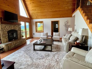 Uma sala de estar ampla com lareira de pedra, um sofá, uma mesa de centro e uma escada.