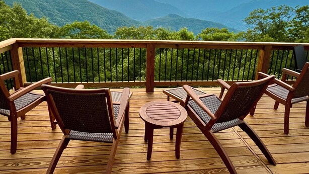 Eine Holzterrasse mit Gartenmöbeln, mit Blick auf eine Berglandschaft.