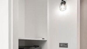 Una habitación de hotel moderna con un refrigerador negro empotrado, una lámpara fijada a la pared y una cama con cabecera.