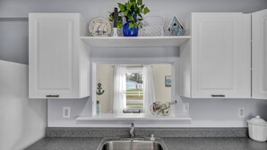 A kitchen with white cabinets, a granite countertop, a stainless steel sink, and a window with a view of a house and greenery.