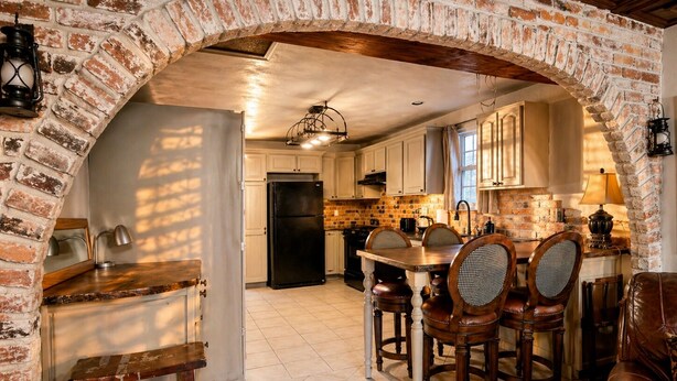 A rustic kitchen with exposed brick walls, a wooden dining table, and a black refrigerator. - Historic Family Escape Near Downtown, Romantic + Pet-Friendly (Wilmington)