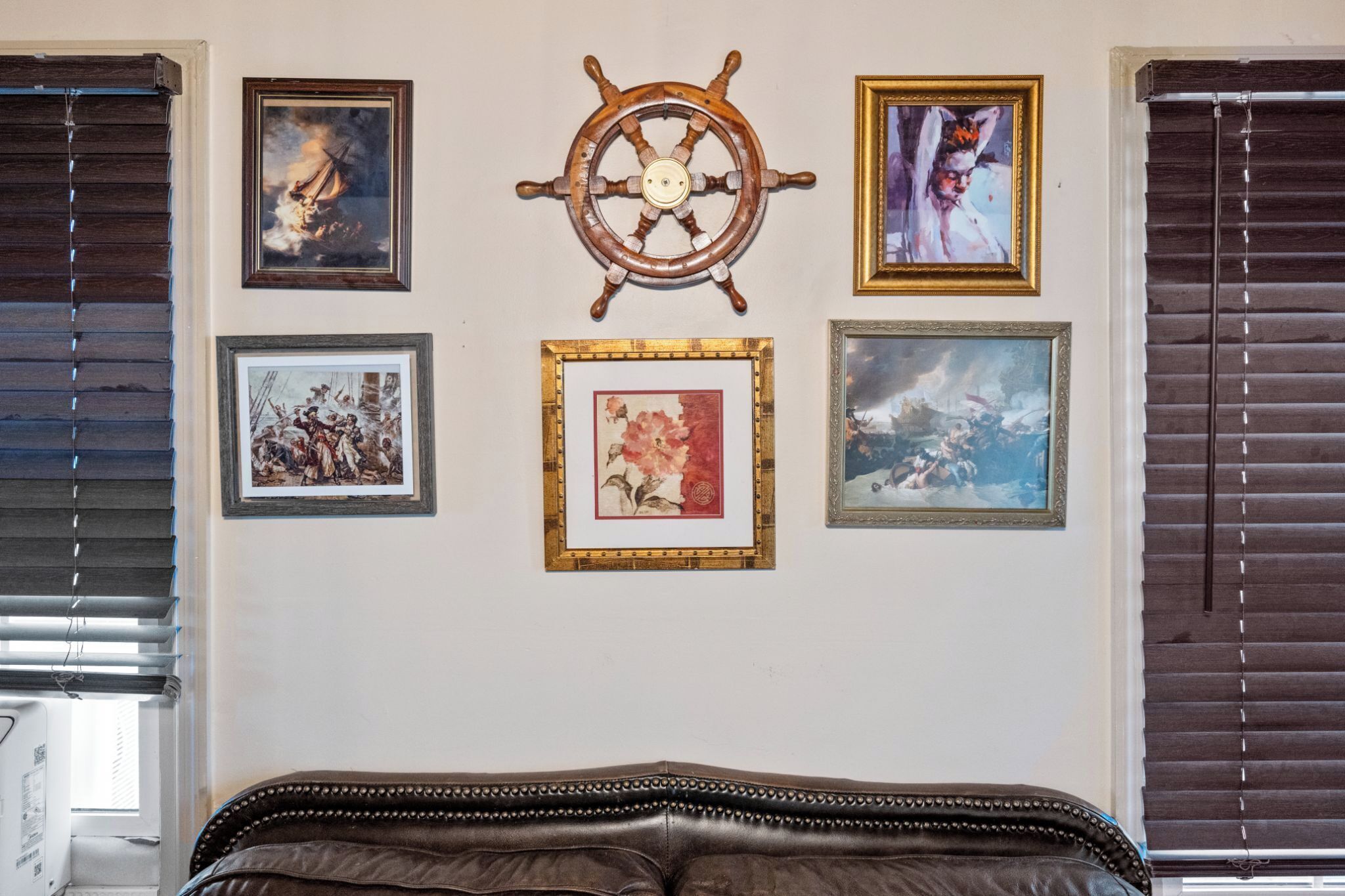 A room with a bed, a wall-mounted ship's wheel, and four framed pictures.