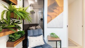 A modern living room with a blue sofa, wooden shelves with plants, a wall clock, and a painting. - Manila Luxury Suites 201 (Medellín)
