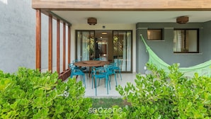 A modern house with a wooden deck, a dining area with blue chairs, and a hammock.