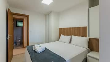 Quarto de hotel com uma cama, mesa de cabeceira, cabeceira de madeira e uma porta que dá para o banheiro.