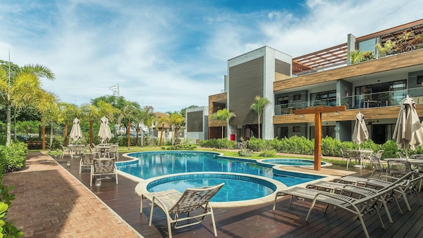 A modern hotel with a central swimming pool, outdoor seating, and lush greenery.