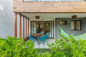 Una casa moderna con terraza de madera, un comedor con sillas azules y una hamaca.