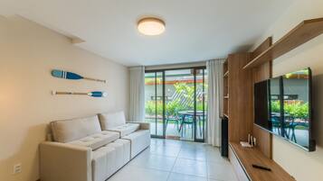 Una sala de estar moderna con un sofá, un televisor de pantalla plana y un ventanal corredizo que da a un patio con mobiliario exterior.