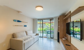 A modern living room with a sofa, a flat-screen TV, and a sliding glass door leading to a patio with outdoor furniture. - Apt in Condo w/ Pool 350m From the Beach Pll0004 (Camaçari)