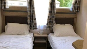Una habitación con dos camas individuales, una mesita de noche pequeña con una taza y cortinas con un estampado de hojas.