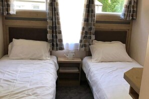 Une chambre avec deux lits simples, une petite table de chevet avec une tasse, et des rideaux à motifs de feuilles.
