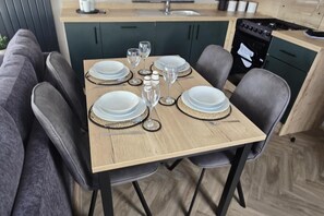 A dining table set with plates, glasses, and cutlery in a modern kitchen with dark cabinets and a wooden floor. - Dove Close 15 Hoburne Devon Bay (Paignton)