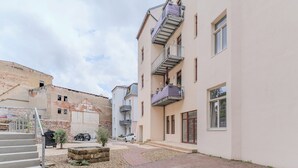 A narrow alleyway between buildings with a paved walkway, a stone wall, and a small garden area.