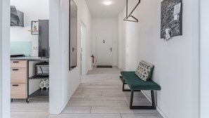 A modern hallway with a bench, a desk with a computer, and a kitchen area.
