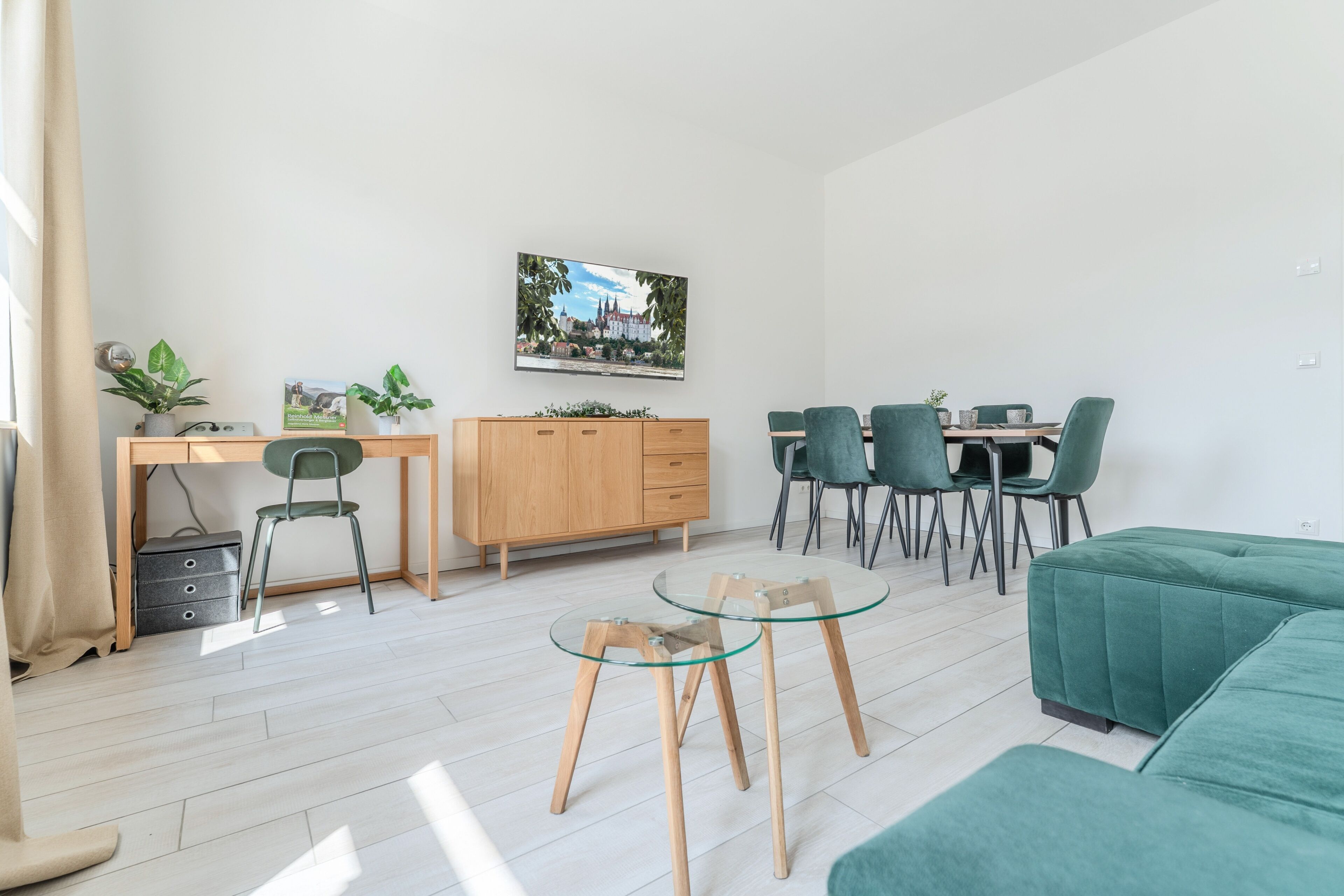 Un salon moderne avec un canapé vert, une table basse en verre et un coin repas comprenant une table et des chaises en bois.