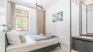 A bedroom with a bed, a window, a painting, and a mirror.