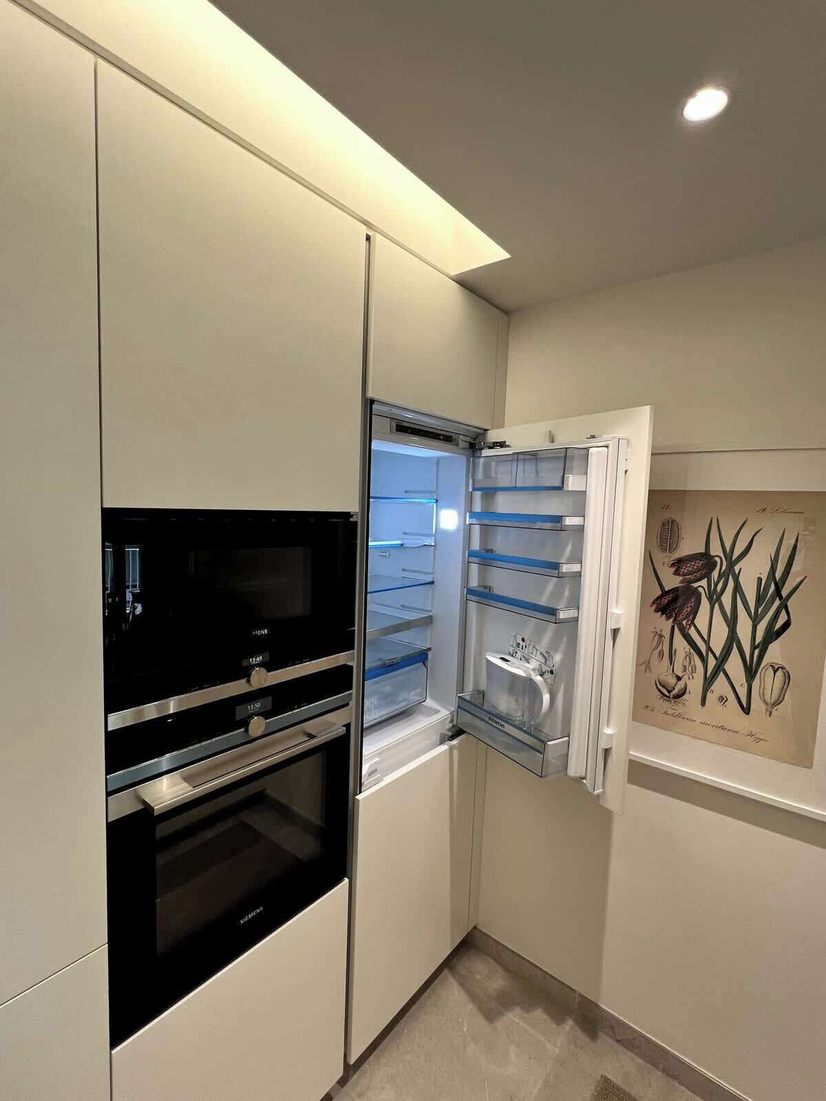 A compact kitchen with a built-in oven, a refrigerator with a freezer, and a wall-mounted artwork.