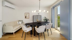 A modern dining area with a round table, white chairs, a black chandelier, and a beige sofa. - Stylish Apartment w/ River View & Terrace (Lisbon)