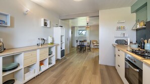 Moderni keittiö, jossa on puiset kaapit, ruokailutila pöytineen ja tuoleineen sekä näkymä viereiseen huoneeseen.