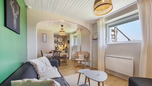 Moderni olohuone, jossa on sohva, pieni pöytä, rottinkituoli ja taustalla ruokailutila.