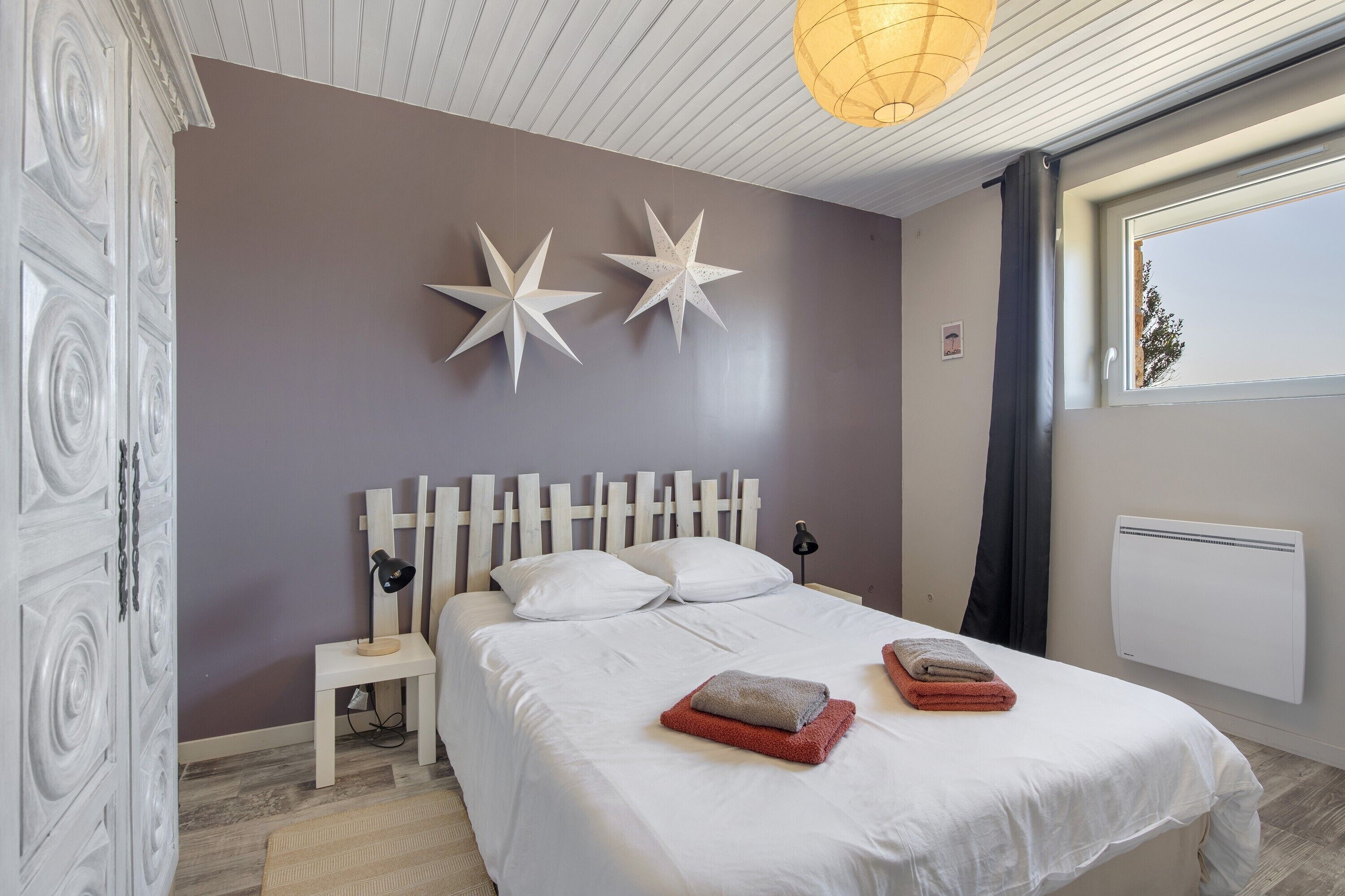 Ein Schlafzimmer mit einem Bett, zwei Sterne-Dekorationen, einem Nachttisch, einer Lampe und einem Fenster mit Vorhängen.