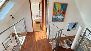 Eine Holztreppe mit Metallgeländern führt zu einem Schlafzimmer mit einem Bett und einem farbenfrohen Gemälde.