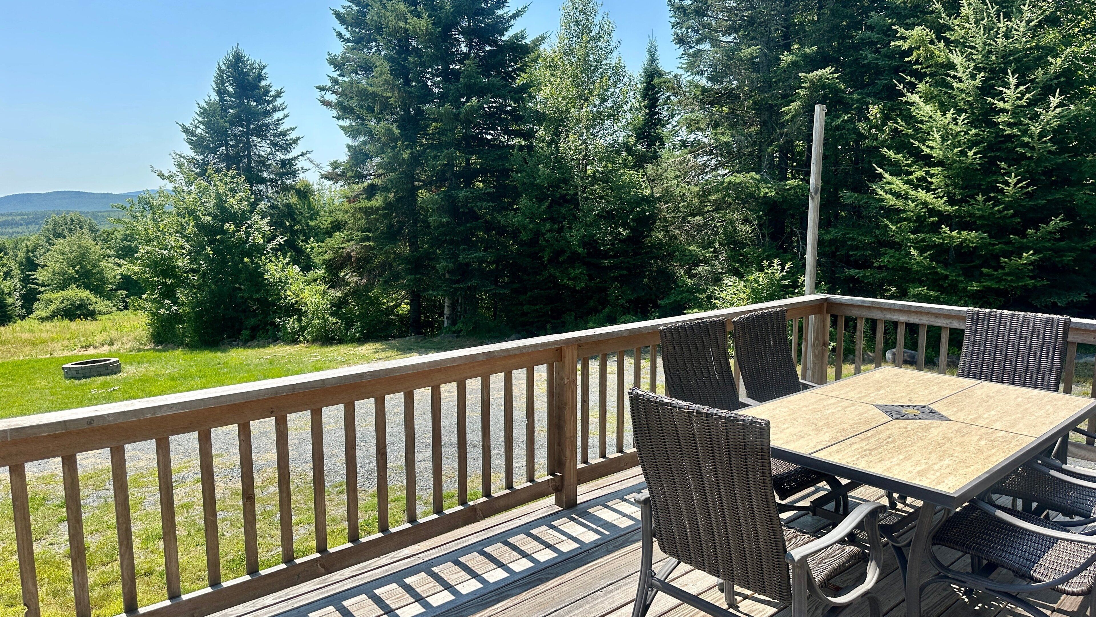 A wooden deck with a table and chairs, surrounded by a wooden railing, overlooking a forested area.