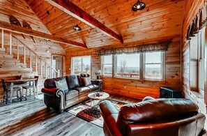 A log cabin interior with a wooden ceiling, a sofa, a dining table, and large windows. - Moosehead State of Mind, 3BR Cabin with Mtn Views & Deck (Shirley)