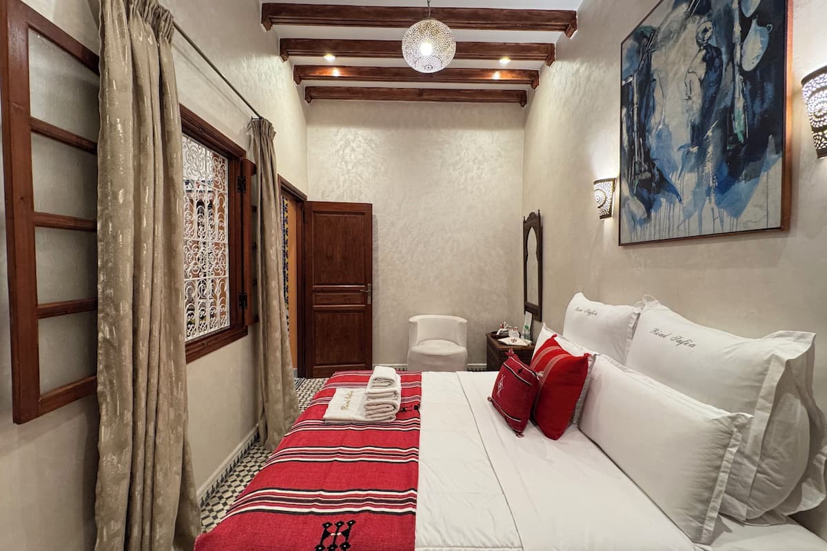 A hotel room with a bed, a chair, a mirror, and a painting on the wall.
