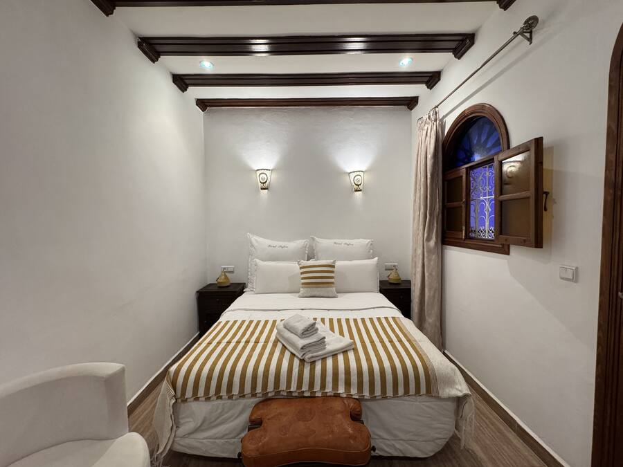 Un dormitorio con una cama, dos mesitas de noche, una lámpara de pared y cortinas en la ventana.
